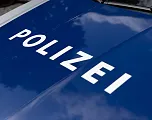 Nahaufnahme einer blauen Motorhaube eines Polizeiwagens mit dem weißen Schriftzug "POLIZEI". Das Licht reflektiert auf der glatten Oberfläche.