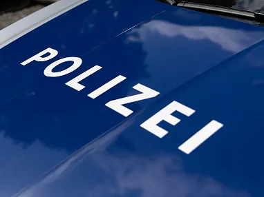 Nahaufnahme einer blauen Motorhaube eines Polizeiwagens mit dem weißen Schriftzug "POLIZEI". Das Licht reflektiert auf der glatten Oberfläche.