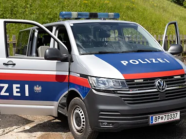 Ein österreichischer Polizeivan mit geöffneten Vordertüren steht auf einer Straße. Das Fahrzeug ist weiß mit blauen und roten Streifen.
