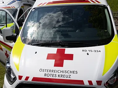 Drei Krankenwagen des Österreichischen Roten Kreuzes stehen nebeneinander auf einer Wiese, bereit für den Einsatz bei Sonnenschein und Wolken am Himmel.