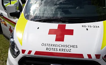 Drei Krankenwagen des Österreichischen Roten Kreuzes stehen nebeneinander auf einer Wiese, bereit für den Einsatz bei Sonnenschein und Wolken am Himmel.