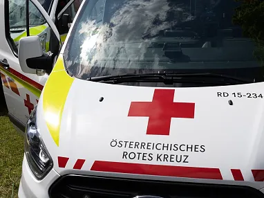 Drei Krankenwagen des Österreichischen Roten Kreuzes stehen nebeneinander auf einer Wiese, bereit für den Einsatz bei Sonnenschein und Wolken am Himmel.