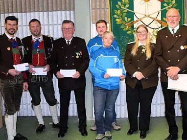 Gruppe von Menschen in traditioneller Tracht und Uniformen in einem Innenraum, einige halten Dokumente. Hintergrund zeigt dekorative Wandtäfelung.
