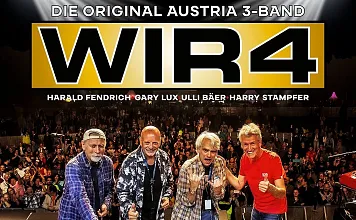 Vier Musiker stehen auf einer Bühne vor einem großen Publikum und posieren lächelnd für die Kamera. Im Hintergrund sieht man den Schriftzug "WIR4".