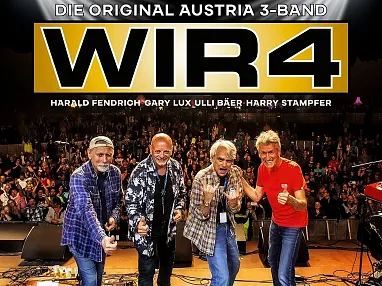 Vier Musiker stehen auf einer Bühne vor einem großen Publikum und posieren lächelnd für die Kamera. Im Hintergrund sieht man den Schriftzug "WIR4".