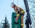 Ein Feuerwehrmann in Schutzkleidung und Helm stapelt Bierkisten draußen. Ein Kran ist im Hintergrund sichtbar. Es ist ein klarer, sonniger Tag.